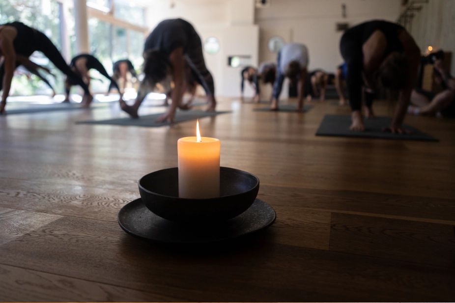 Kerze auf dem Holzboden, im Hintergrund eine Gruppe in der Yoga-Praxis